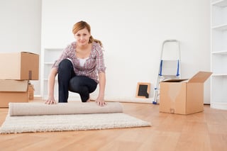 Pretty blonde woman rolling up a carpet to prepare to move house.jpeg